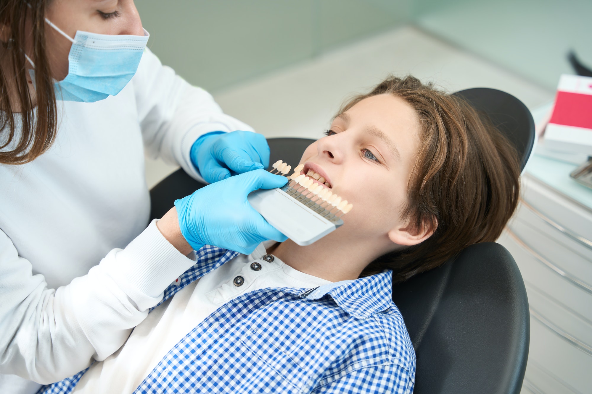 Woman doctor picks up color of tooth to teenager boy