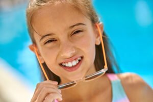 A smiling child, holding sunglasses, embodies the joy of holidays and healthy teeth, illustrating Holiday Dental Tips For Kids