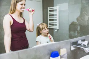 A woman and child brush their teeth, considering an Electric Toothbrush for Children in Beverly Hills.